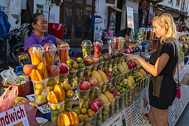 Young blonde woman at a market stall on Sisavangvong Road (the main street) which sells freshly squeezed fruit juice, Luang Prabang, Luang Prabang Province, Laos, Asia