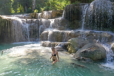 Aerial view of a beautiful young blonde woman wading through the natural pools of the magnificent Kuang Si Falls, Kuang Si, Luang Prabang Province, Laos, Asia