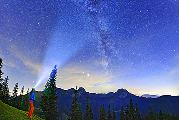 Woman stands at Farrenpoint and shines with lamp on starry sky with Milky Way, Farrenpoint, Mangfall Mountains, Bavarian Alps, Upper Bavaria, Bavaria, Germany