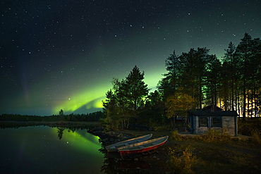 Northern lights in the night sky on the lakeshore with hut and boats in Lapland, Sweden