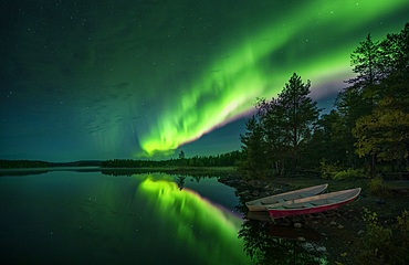 Northern lights in the night sky on the lake shore with boats in Lapland, Sweden