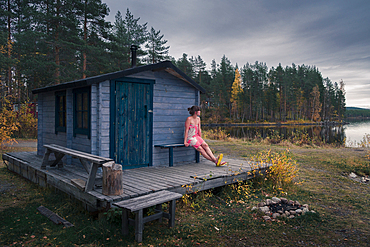 Woman sitting in front of sauna by the lake in Lapland, Sweden