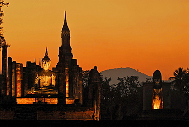 Illuminated Buddha in evening light with orange coloured sky at Wat Mahathat, Sukothai Historical Park, Central Thailand, Asia