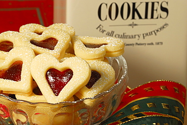 Christmas cookies raspberry hearts covered with sugar piling up in glasbowl, Christmas decoration in background