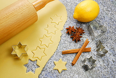 Stars cutted out of cookies dough, cookie cutters for Christmas cookies, rolling pin, lemon, cinnamon and star anise laying at worktop