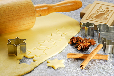 Stars cutted out of cookies dough, cookie cutters for Christmas cookies, rolling pin, wood pattern, cinnamon and star anise laying at worktop