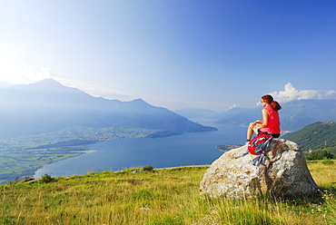 Woman sitting on rock while looking over Lake Como, Monti Lariani, Lombardy, Italy