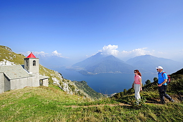 Two hikers near San Bernardo chapel, Monti Lariani, Lake Como in background, Lombardy, Italy