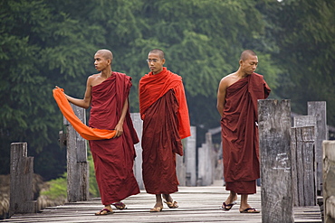 Three young buddhistic monks walking on the U Beins Bridgein Amarapura near Mandalay, Myanmar, Burma