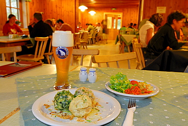 laid table with one portion of Tyrolean Knoedel, Spinatknoedel, Kasknoedel and Speckknoedel, mixed salad and weissbier, guests at tables out of focus in background, hut Franz-Senn-Huette, Stubaier Alpen range, Stubai, Tyrol, Austria