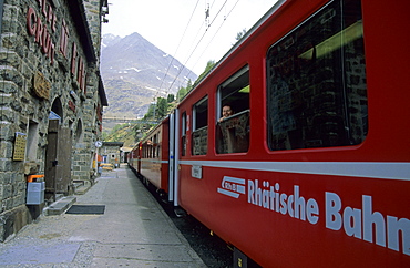 Woman smiling out of window of red train of Rhaetische Bahn at station Alpe Gruem, Alp Gruem, Ferrovia Raetia, Bernina range, Bernina, Puschlav, Grisons, Switzerland