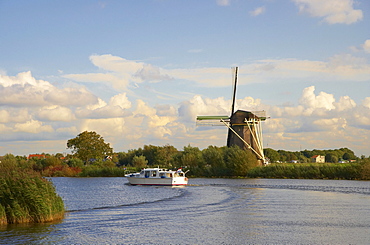 A motorboat on the river Vecht driving past a windmill, Netherlands, Europe
