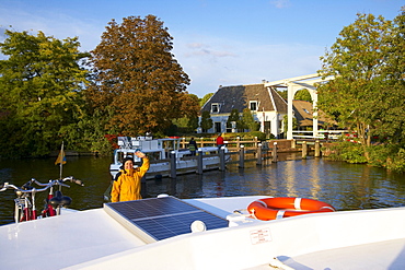 Waving woman on a houseboat on the river Vecht, bascule bridge in the background, Netherlands, Europe