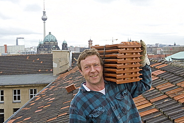 portrait, roof tiler carrying tiles on shoulder, on roof, Berlin skyline in background, Berlin, Germany