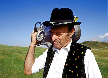 A man wearing traditional costume carrying a milk can on his shoulder, South Tyrol, Italy, Europe