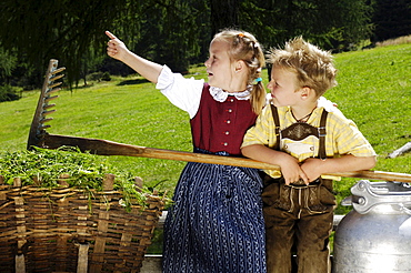 Girl and boy wearing traditional clothes with basket and milk can, Alpine meadow, Agriculture, South Tyrol, Italy