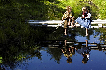 Boy and girl in traditional dress sitting on a wooden jetty at a lake, Alp, South Tyrol, Italy