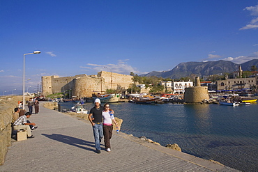 A couple walking along the promenade, Kyrenia harbour and Kyrenia castle, Kyrenia, Girne, North Cyprus, Cyprus