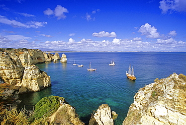 Sailing ships off the rocky coast under clouded sky, Ponta da Piedade, Algarve, Portugal, Europe