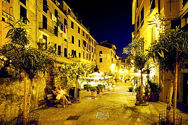 Couple sitting on a bench in front of illuminated restaurants, Vernazza, Cinque Terre, Liguria, Italian Riviera, Italy, Europe