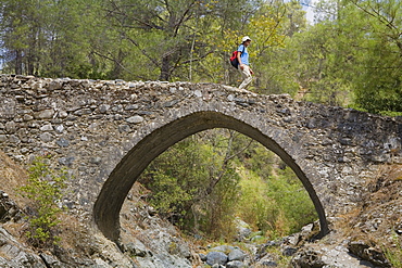 A hiker walking over a stone bridge, Elaia bridge, Diarizos Valley, near Pafos, Cyprus