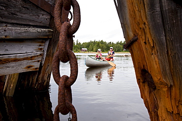 A girl and a woman in a canoe between ship wrecks on the island of Norrbyskaer, Vaesterbotten, Sweden, Europe