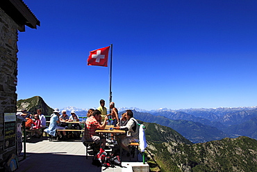 Hikers having a rest in front of mountain scenery at Capanna Tamaro hut, mountain hike to Monte Tamaro, Ticino, Switzerland