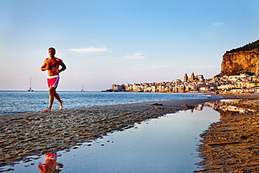 Jogger at beach, old town, cathedral and cliff La Rocca, Cefal?, Palermo, Sicily, Italy