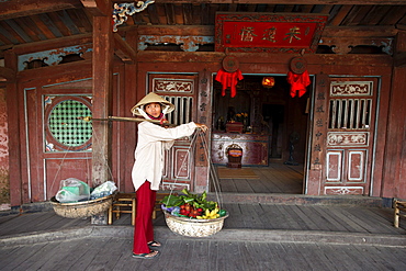 Woman with baskets passing Chua Cau, Japanese Bridge, Hoi An, Annam, Vietnam