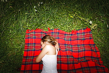 Young woman lying on red checked blanket on grass