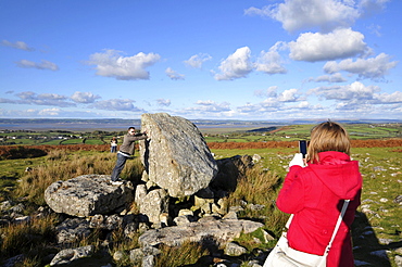 Young women taking a photo of boyfriend pushing stone, King Arthurs Stone, Cefn Bryn, Gower peninsula, south-Wales, Wales, Great Britain