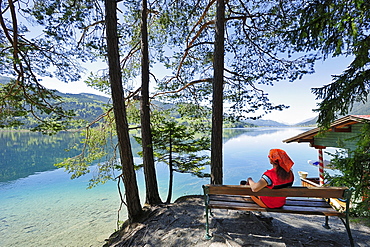 Woman sitting on wooden bench and enjoying view of lake Weissensee, lake Weissensee, Carinthia, Austria, Europe