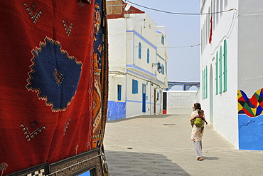 Carpet and woman carrying a baby on her back in the old town of Asilah, Atlantic Coast, Morocco, Africa