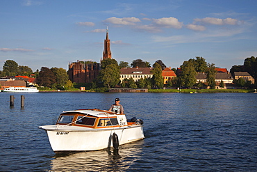 Fisherman in motorboat, view over Fleesensee lake to Malchow monastery, Mueritz-Elde-canal, Mecklenburg lake district, Mecklenburg Western-Pomerania, Germany, Europe
