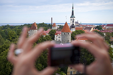 Hands hold compact camera to capture overhead of city with churches and towers from Toompea hill, Tallinn, Harjumaa, Estonia