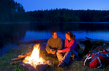 Young couple sitting at a campfire in the evening, lake Ottenstein, Lower Austria, Austria, Europe