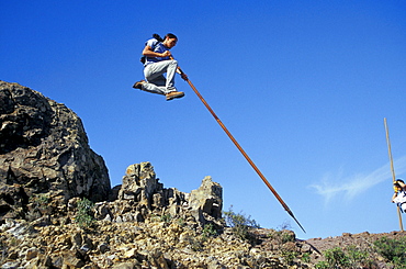 Man leeping over rocks with a Canarian shepherd stick, Canary Islands, Spain