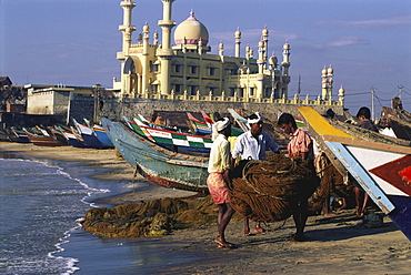 Fishermen and boats on the beach in front of mosque, Kovalam, Kerala, India