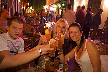 Young people toasting with drinks in an open-air bar at night, Kos-Town, Kos, Greece