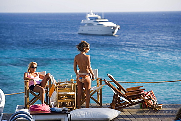 Women in the Goya Beach Bar, the only beach bar with pool, watching to a yacht at sea, Paranga Beach, Mykonos, Greece