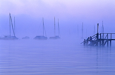 Europe, Germany, Bavaria, near Riederau, Lake Ammer, Sailing boats and people on the gangplank in the haze