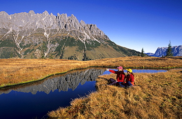 two hikers at lake on Hochkeil, view to Bratschenkopf, Manndlwand, Hochkoenig area, Barchtesgaden range, Salzburg, Austria