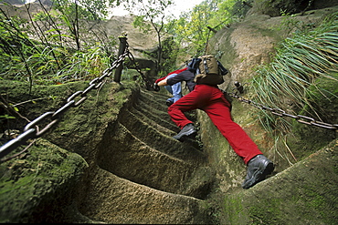 western tourist on steep pilgrim path along stone steps with worn down chain handrail, Hua Shan, Shaanxi province, Taoist mountain, China, Asia