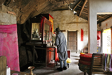 A monk standing in front of the altar of a cave temple, Jiuhuashan, Anhui province, China, Asia