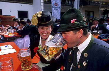 Young couple in dirndl dress and traditional dress, saying cheers in a beer garden, pilgrimage to Raiten, Schleching, Chiemgau, Upper Bavaria, Bavaria, Germany