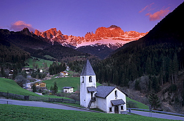 Church of St. Zyprian with range of Tschaminspitzen, Vajoletttuerme and Koeniglaurinwand in alpenglow, Dolomites, South Tyrol, Italy