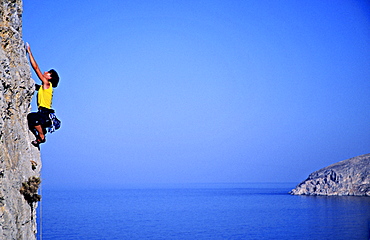 Kalymnos, Greece a woman climbs on a vertical rock pillar above the Aegean Sea, Europe, MR