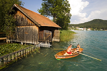 Young couple in a rowboat on Lake Faak near a boathouse, Carinthia, Austria