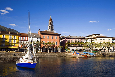 Sailling boat on Lake Maggiore, harbour promenade with spire of church Santi Pietro Paolo in background, Ascona, Ticino, Switzerland