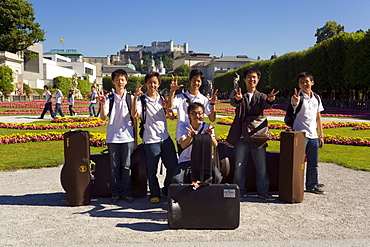 Members of the Asian Youth Orchestra smiling at camera, Mirabell castle and garden, Hohensalzburg Fortress, largest, fully-preserved fortress in central Europe, in background, Salzburg, Salzburg, Austria